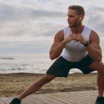 Hombre joven con cascos y ropa deportiva estirando antes de hacer deporte.