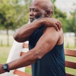 Hombre de mediana edad de color se toca la parte de atrás del hombro con gesto de dolor