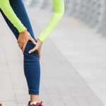 Mujer joven, con ropa deportiva, se sujeta la rodilla por un dolor fuerte o una rotura del menisco.
