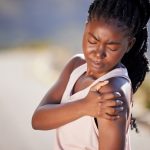 Atleta de color se coge el hombro con expresióm de dolor
