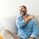 Hombre con barba tocandose el hombro con expresión de dolor